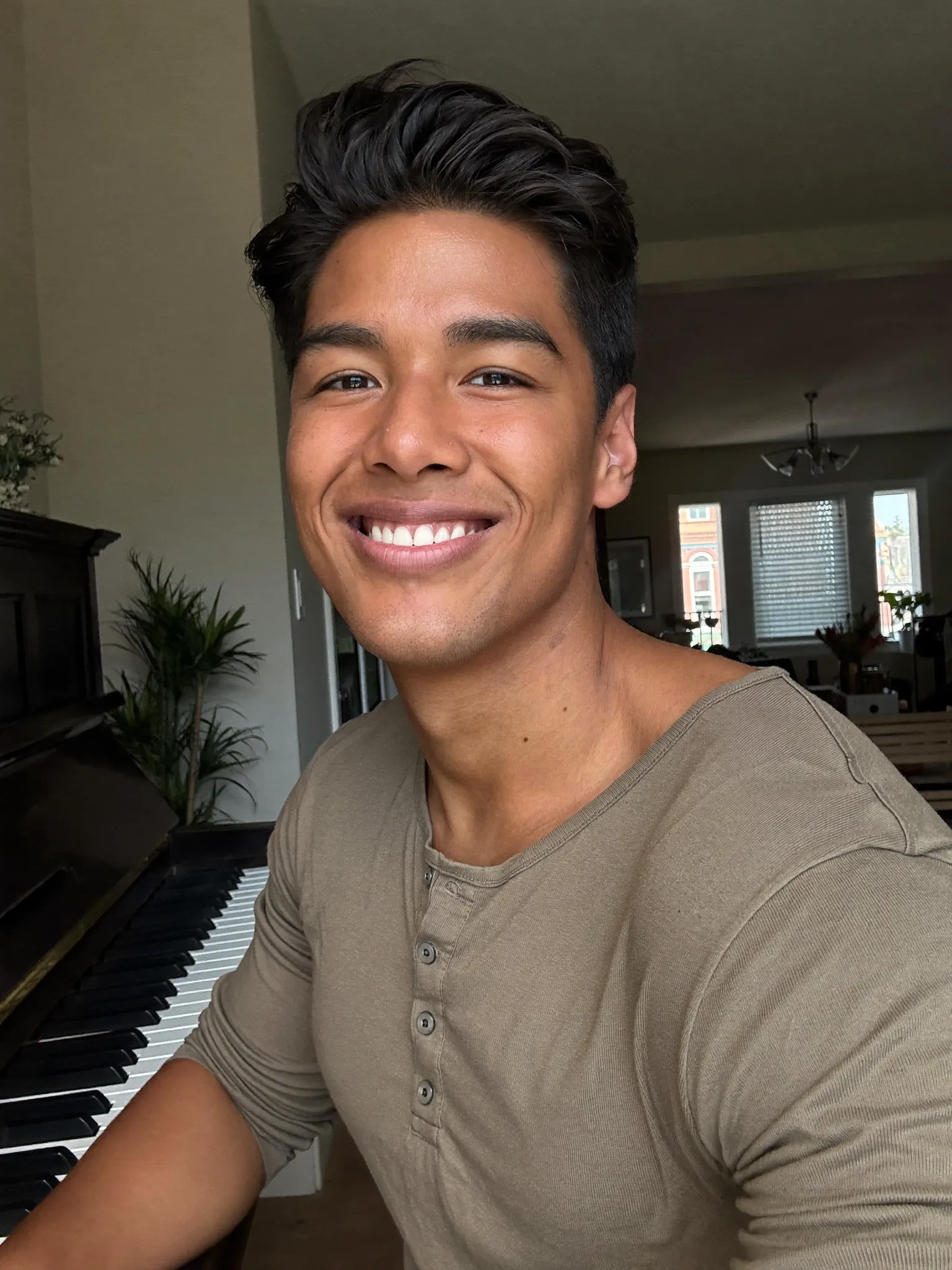 Christian smiling at a piano in his sunlit living room