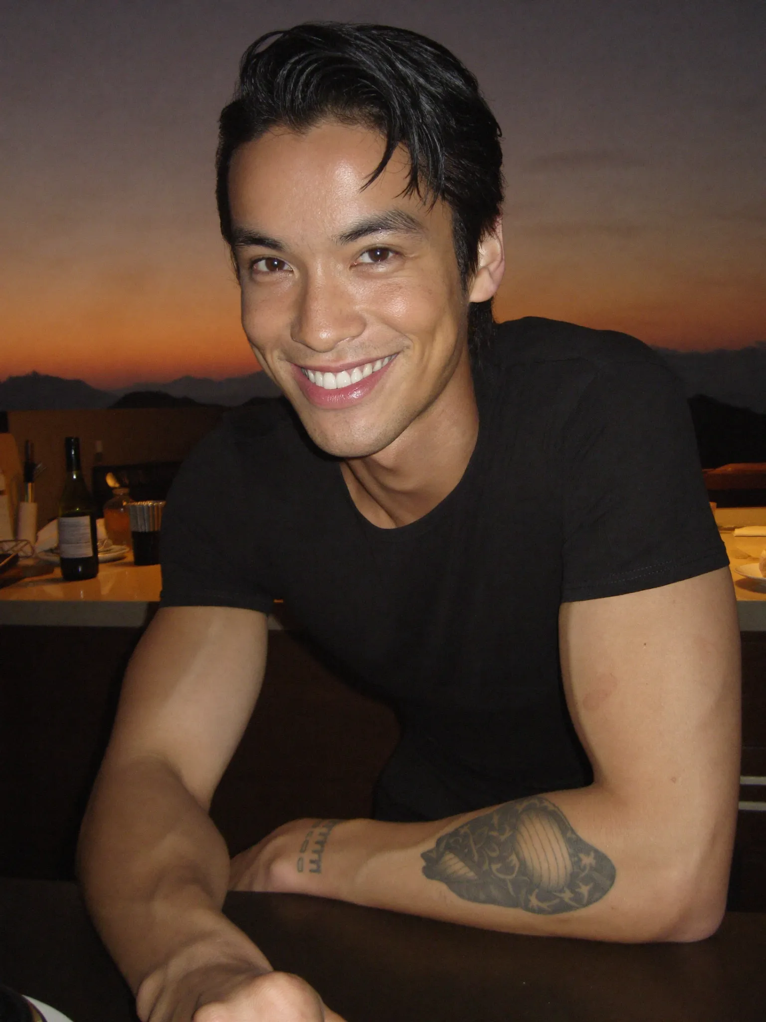 Danny smiling at a table with a sunset sky behind him