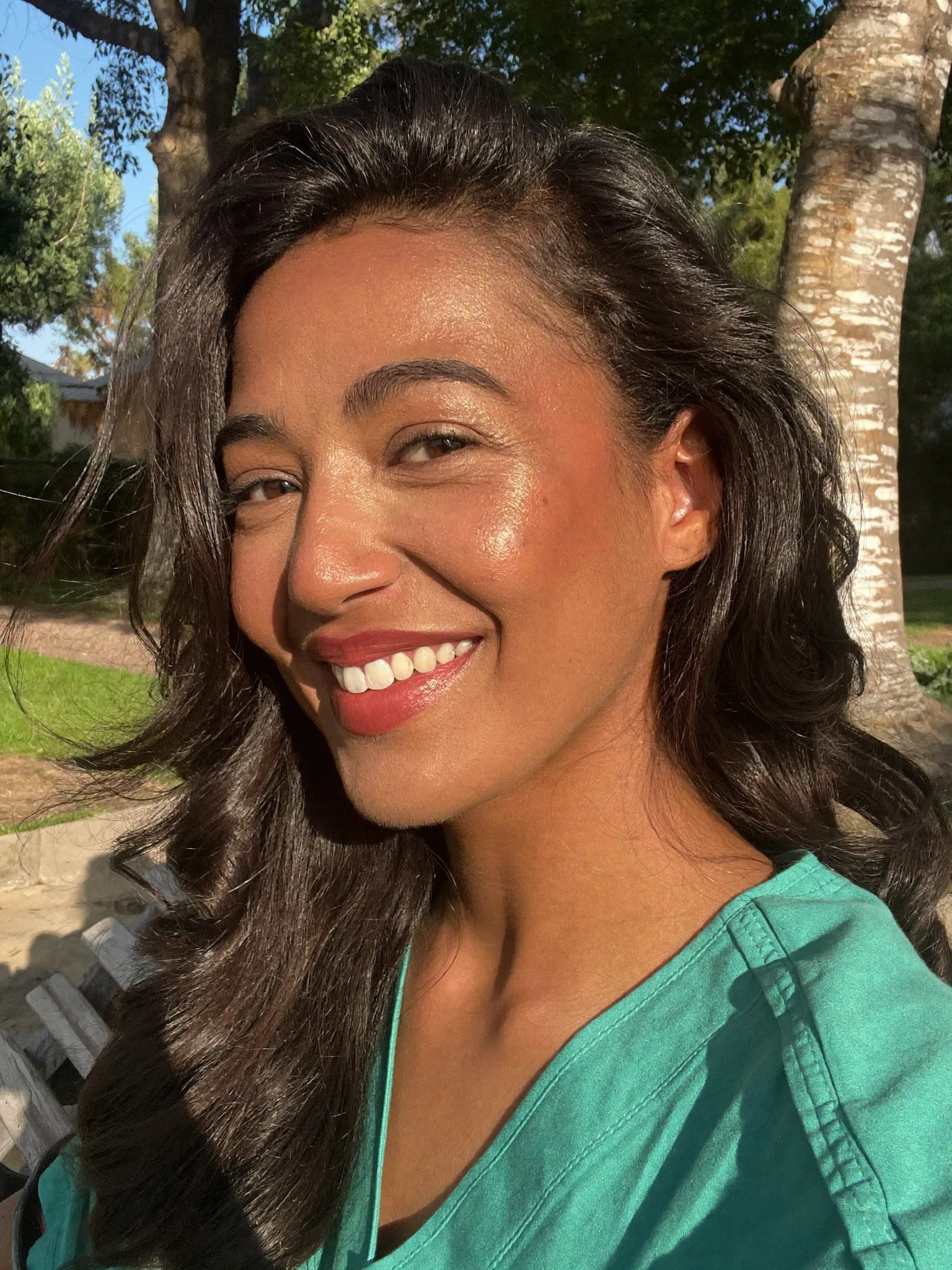 Selam smiling in green scrubs under a tree on a sunny day